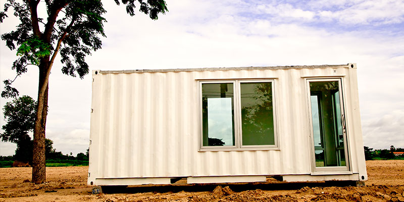 A solo white container office is kept under a tree.